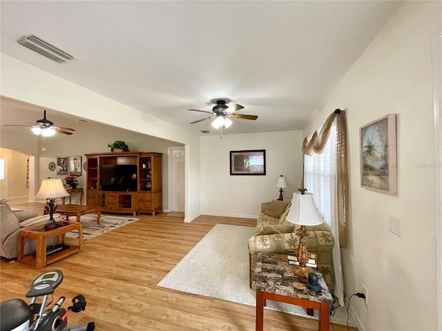 living room featuring baseboards, light wood finished floors, visible vents, and a ceiling fan