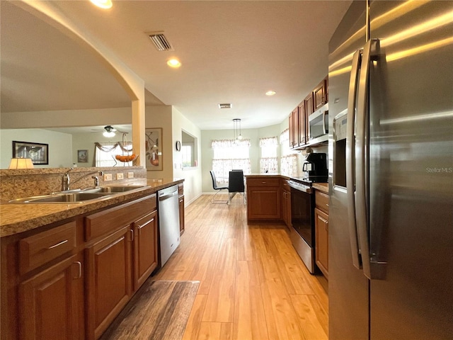 kitchen with a peninsula, a sink, visible vents, light wood-style floors, and appliances with stainless steel finishes