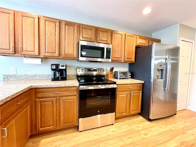 kitchen featuring appliances with stainless steel finishes, brown cabinets, light countertops, and light wood-style floors