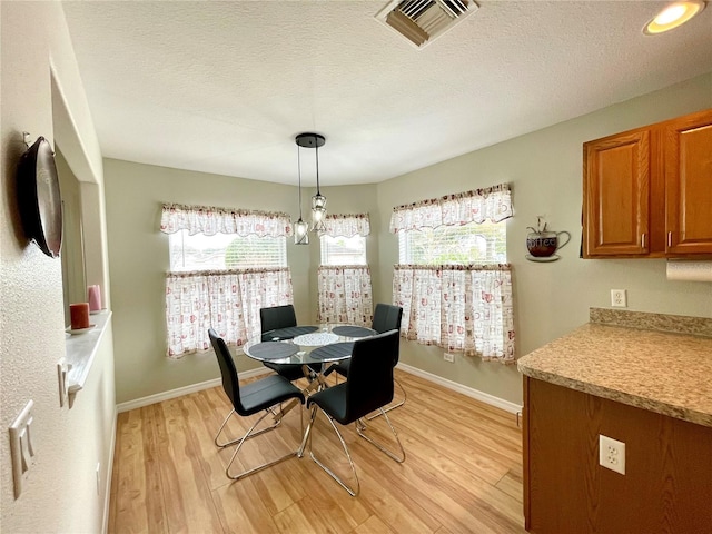 dining area with light wood-style floors, visible vents, plenty of natural light, and a textured ceiling