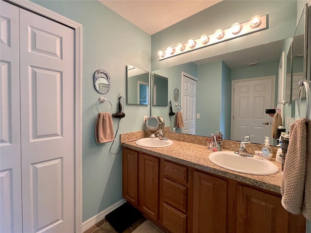 full bath with tile patterned flooring, a sink, baseboards, and double vanity