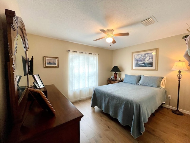 bedroom with a textured ceiling, ceiling fan, wood finished floors, and visible vents