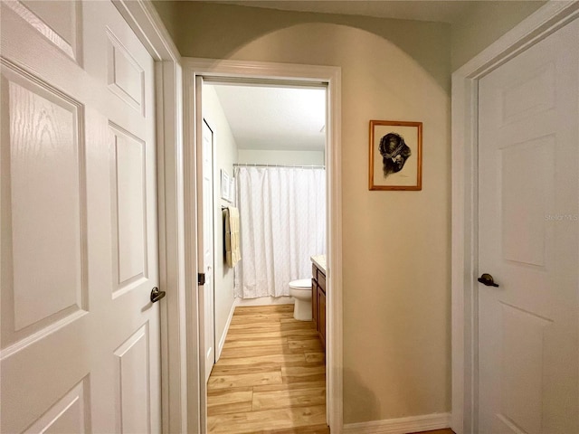 hallway featuring arched walkways, baseboards, and light wood finished floors