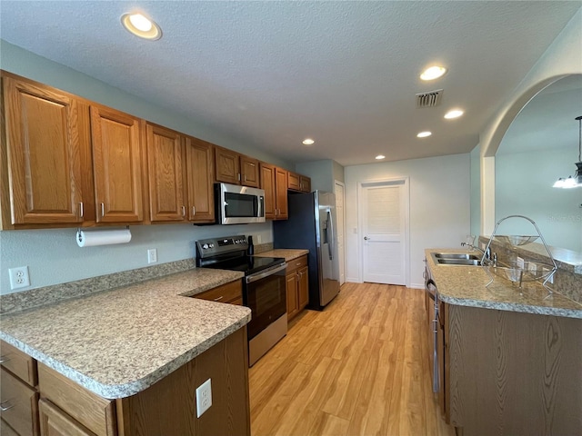 kitchen with a peninsula, light wood-style flooring, stainless steel appliances, and a sink