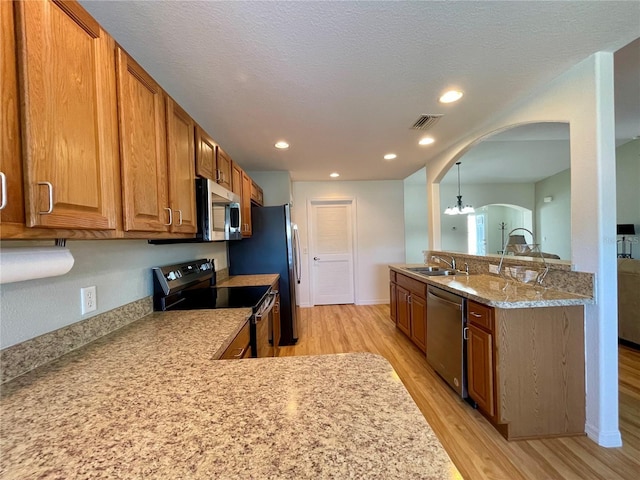 kitchen featuring arched walkways, stainless steel appliances, visible vents, brown cabinetry, and a sink