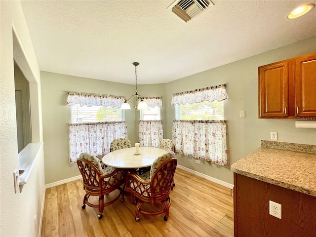 dining space with baseboards, visible vents, a textured ceiling, and light wood finished floors