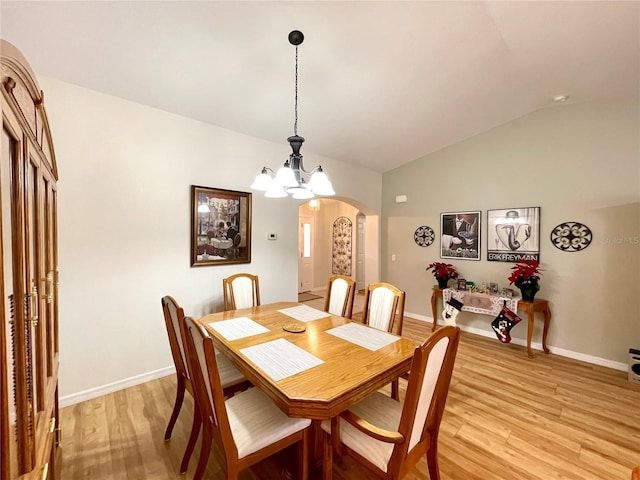 dining space featuring arched walkways, a notable chandelier, vaulted ceiling, light wood-type flooring, and baseboards