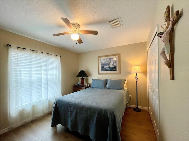 bedroom with ceiling fan, wood finished floors, visible vents, and baseboards