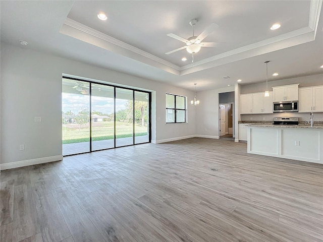 unfurnished living room with ceiling fan with notable chandelier, a raised ceiling, sink, light hardwood / wood-style flooring, and ornamental molding