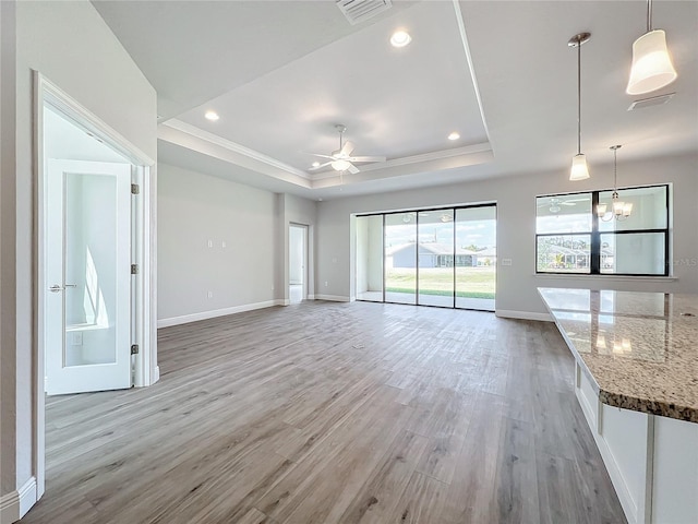 unfurnished living room with ceiling fan with notable chandelier, light hardwood / wood-style floors, and a tray ceiling