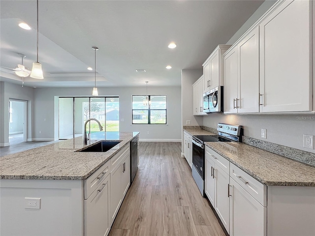 kitchen with stainless steel appliances, a kitchen island with sink, sink, decorative light fixtures, and white cabinets