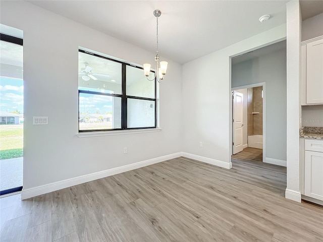 unfurnished dining area featuring ceiling fan with notable chandelier and light hardwood / wood-style flooring