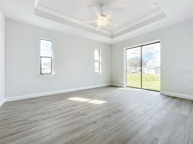 empty room with ceiling fan, light wood-type flooring, crown molding, and a tray ceiling