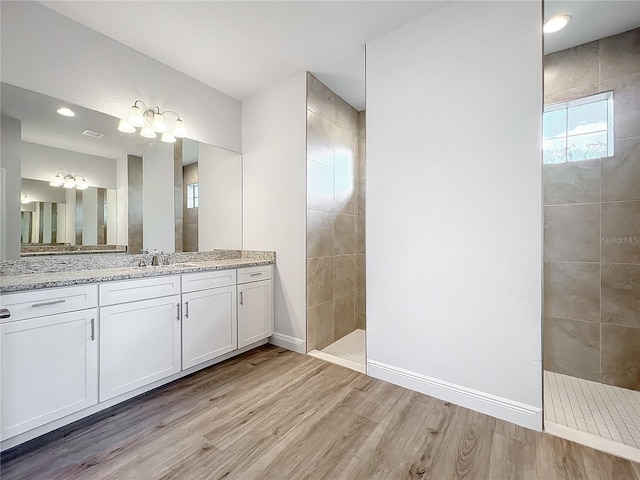 bathroom featuring vanity, a tile shower, and wood-type flooring