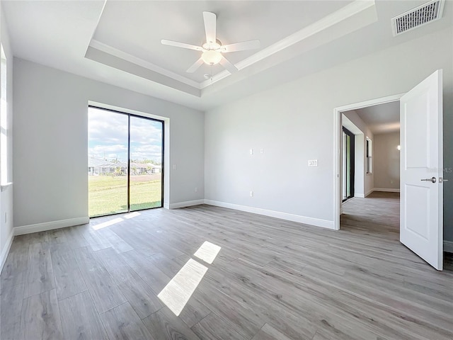 unfurnished room featuring a raised ceiling, ceiling fan, and light wood-type flooring