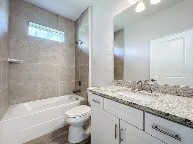 full bathroom featuring hardwood / wood-style floors, vanity, tiled shower / bath combo, and toilet