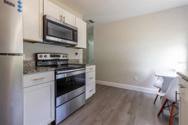 kitchen featuring dark stone countertops, white cabinetry, light wood-type flooring, and appliances with stainless steel finishes