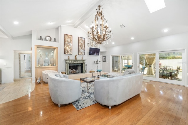 living room with a skylight, a notable chandelier, beamed ceiling, light hardwood / wood-style floors, and a tiled fireplace