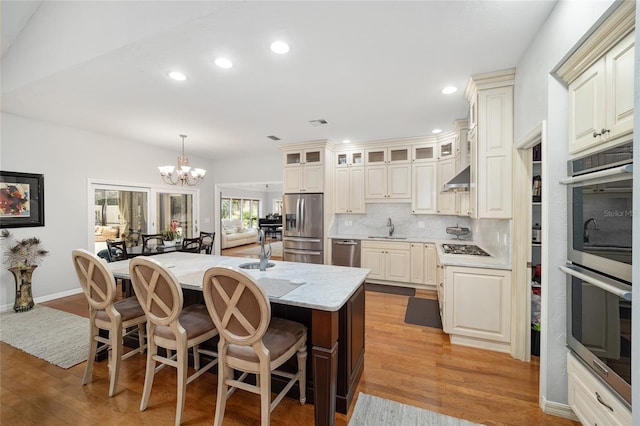 kitchen with light stone countertops, appliances with stainless steel finishes, backsplash, a kitchen island with sink, and light hardwood / wood-style floors