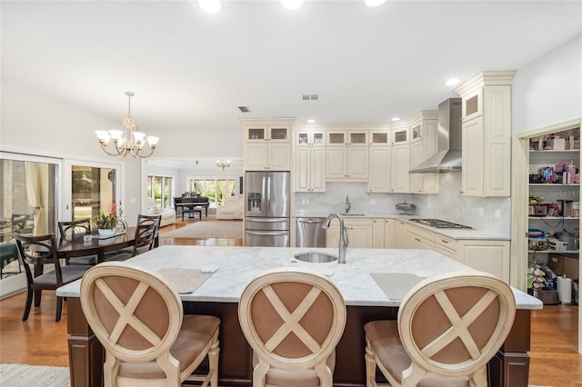 kitchen with sink, wall chimney range hood, pendant lighting, a spacious island, and appliances with stainless steel finishes