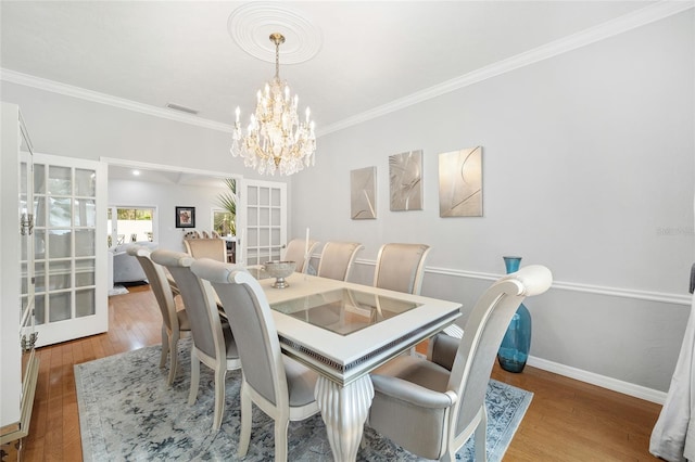 dining space featuring french doors, ornamental molding, a notable chandelier, and light wood-type flooring