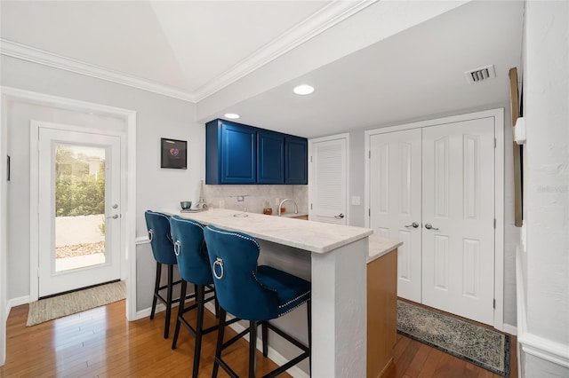 kitchen featuring wood-type flooring, a kitchen bar, kitchen peninsula, and blue cabinetry