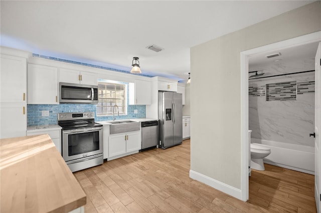 kitchen featuring appliances with stainless steel finishes, tasteful backsplash, sink, light hardwood / wood-style flooring, and white cabinets