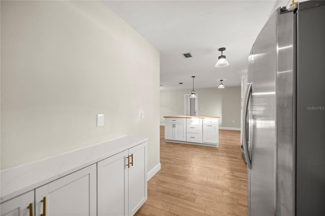 kitchen featuring pendant lighting, white cabinetry, stainless steel refrigerator, and light hardwood / wood-style floors