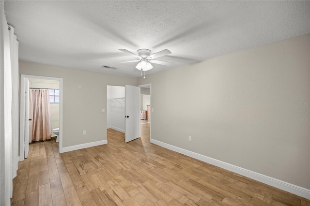 unfurnished bedroom with a textured ceiling, light wood-type flooring, ensuite bathroom, and ceiling fan