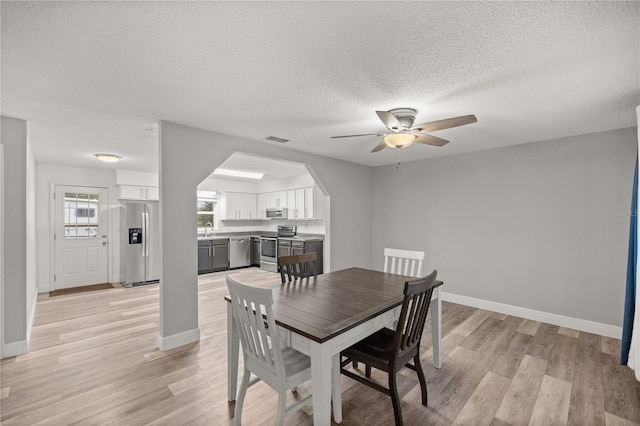 dining space featuring ceiling fan, light wood-type flooring, sink, and a textured ceiling