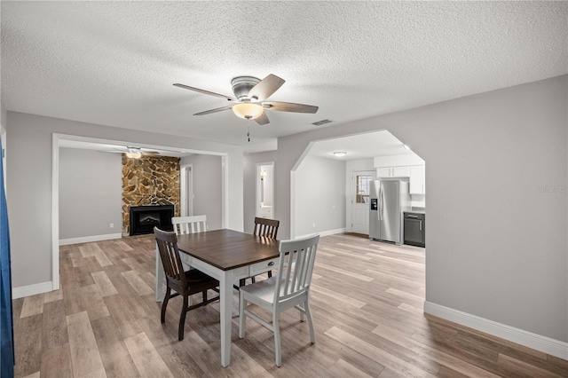 dining area with ceiling fan, a stone fireplace, and light hardwood / wood-style floors