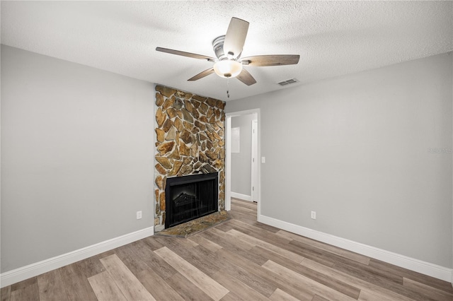 unfurnished living room featuring ceiling fan, a textured ceiling, light hardwood / wood-style flooring, and a fireplace