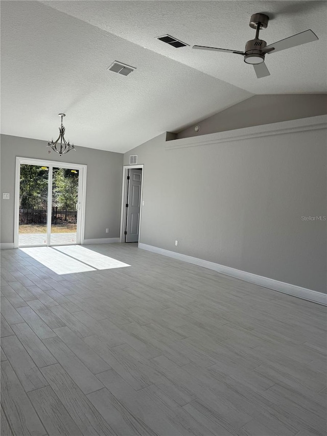 empty room featuring ceiling fan with notable chandelier, light wood-type flooring, a textured ceiling, and vaulted ceiling