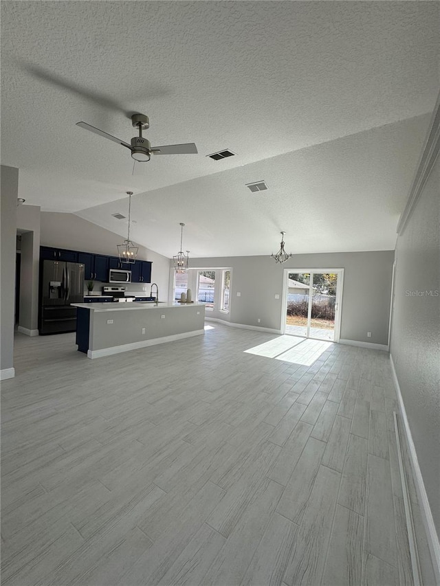 unfurnished living room featuring ceiling fan with notable chandelier, light wood-type flooring, lofted ceiling, and a textured ceiling