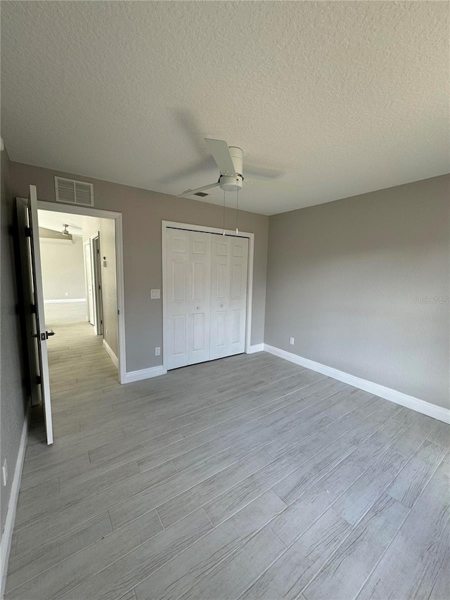 unfurnished bedroom with a textured ceiling, light wood-type flooring, a closet, and ceiling fan