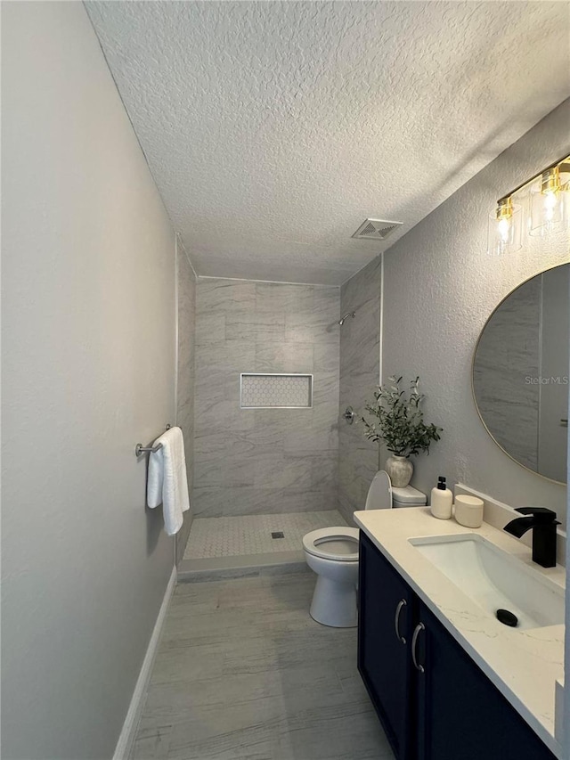 bathroom with tiled shower, vanity, a textured ceiling, and toilet