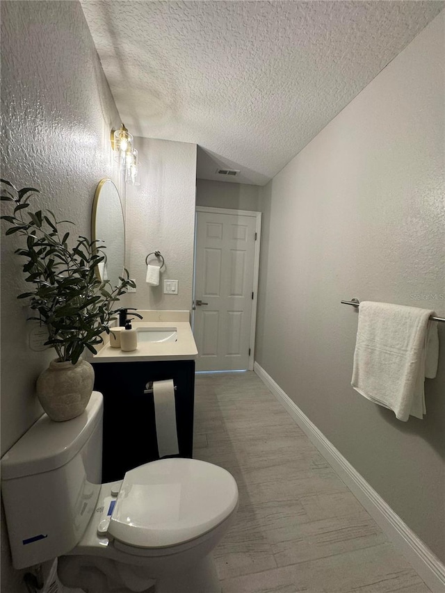 bathroom featuring vanity, hardwood / wood-style floors, a textured ceiling, and toilet