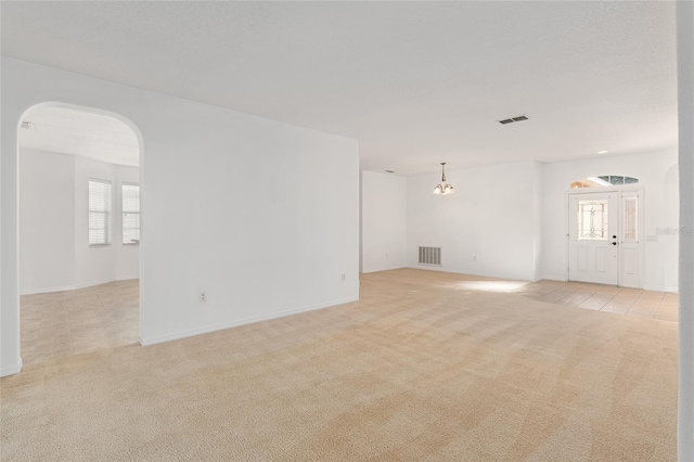 spare room with light colored carpet and an inviting chandelier