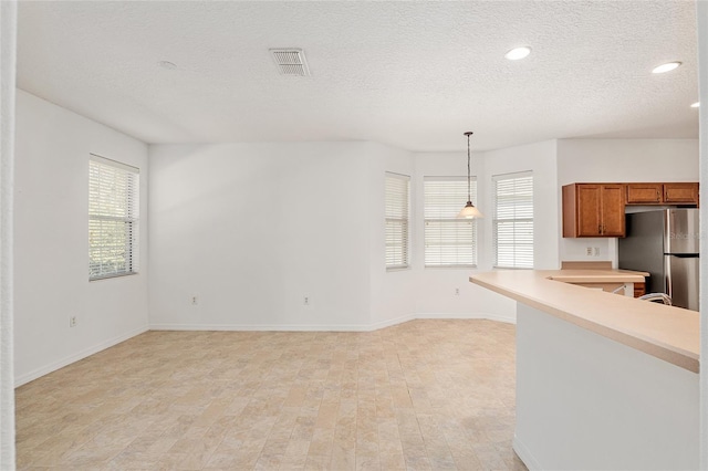 kitchen featuring stainless steel refrigerator, kitchen peninsula, pendant lighting, and a textured ceiling