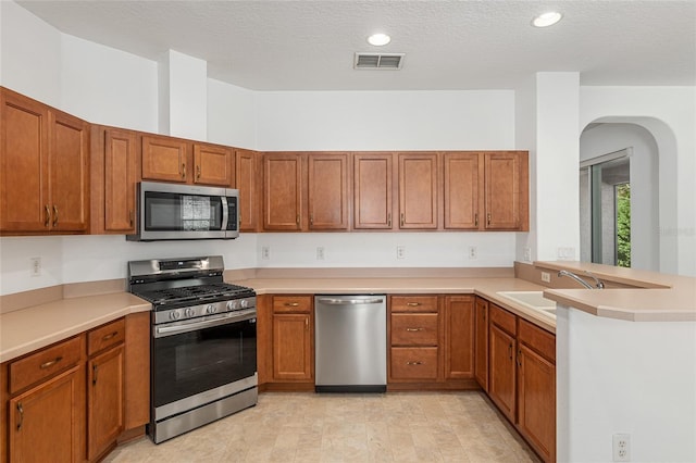 kitchen featuring a textured ceiling, kitchen peninsula, sink, and appliances with stainless steel finishes