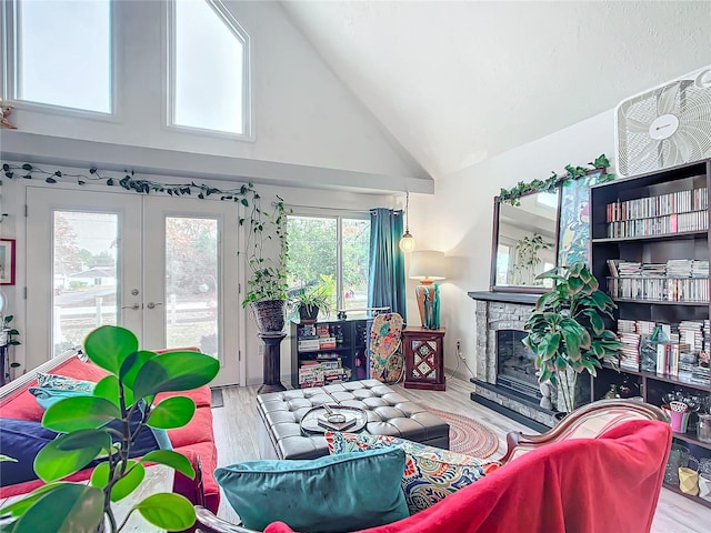 living room with light wood-type flooring, high vaulted ceiling, a wealth of natural light, and a stone fireplace