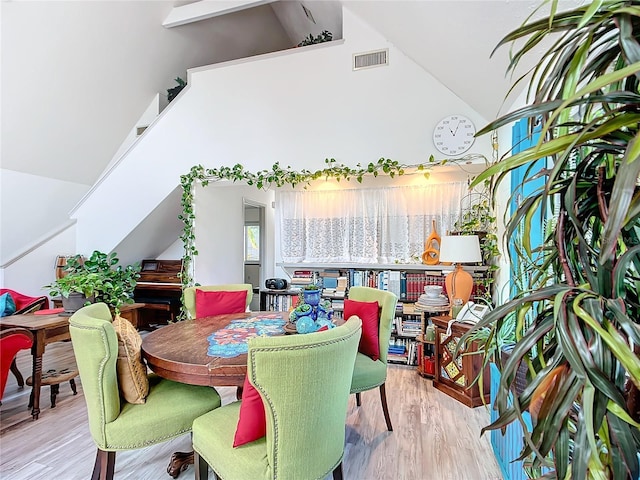 dining space with high vaulted ceiling and light hardwood / wood-style flooring