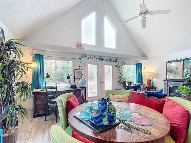 dining room with french doors, ceiling fan, high vaulted ceiling, light hardwood / wood-style floors, and a stone fireplace