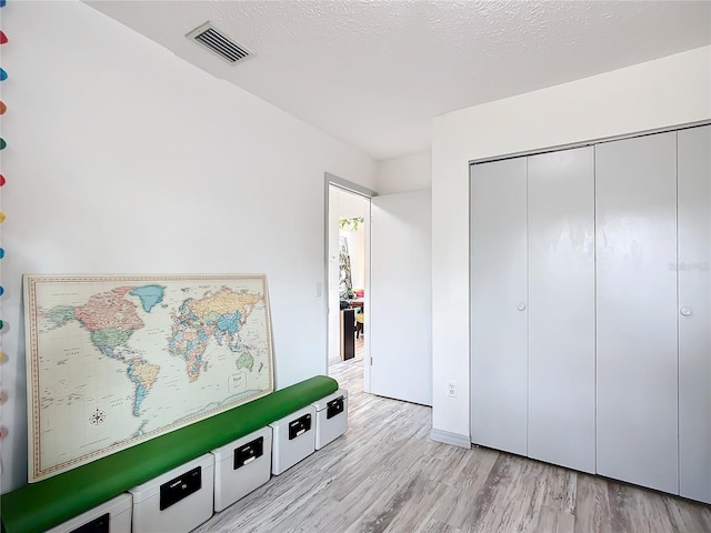 bedroom featuring a closet, light hardwood / wood-style flooring, and a textured ceiling