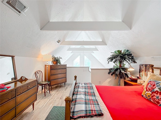 bedroom featuring light wood-type flooring, a textured ceiling, and lofted ceiling