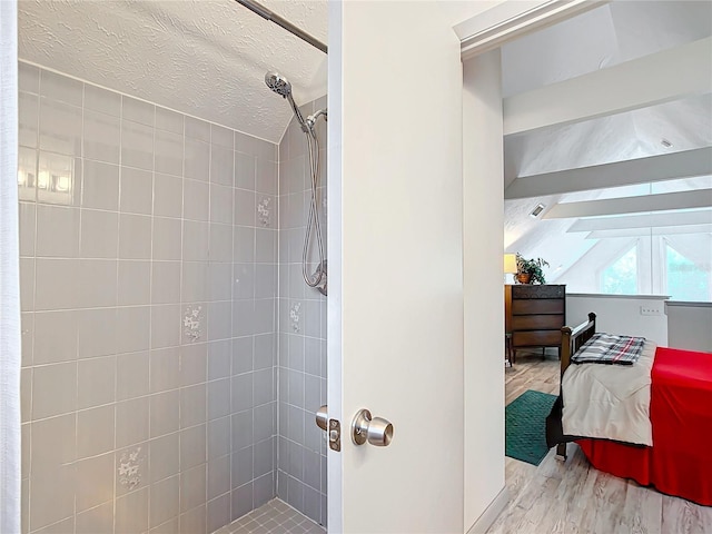 bathroom featuring tiled shower, a textured ceiling, hardwood / wood-style flooring, and vaulted ceiling