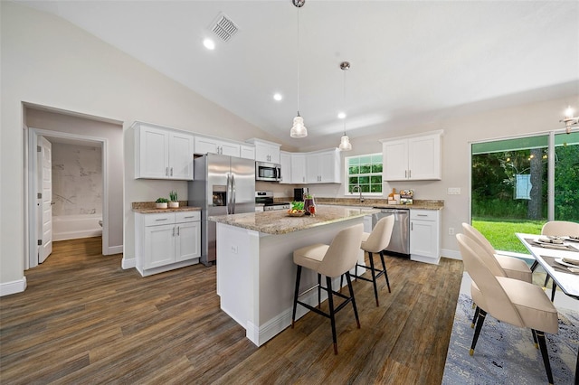 kitchen with lofted ceiling, white cabinets, appliances with stainless steel finishes, decorative light fixtures, and a kitchen island