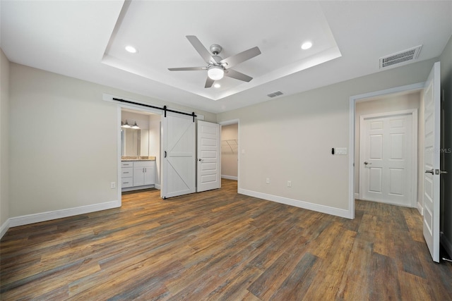 unfurnished bedroom with ceiling fan, a spacious closet, a barn door, dark hardwood / wood-style flooring, and ensuite bathroom