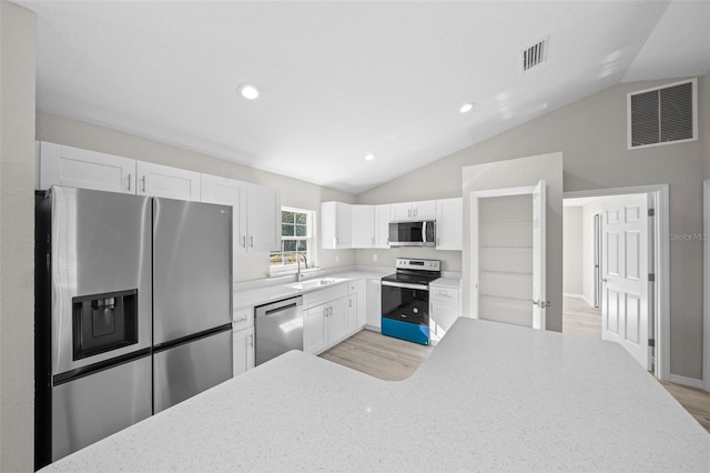 kitchen with stainless steel appliances, white cabinetry, lofted ceiling, and sink