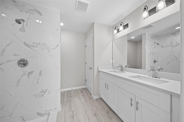 bathroom with wood-type flooring, vanity, and a tile shower